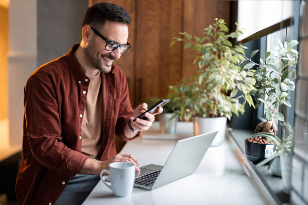 Man using phone and laptop at home, exploring features of landline and mobile Internet in Dubai.