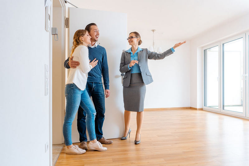 A real estate agent shows a couple a bright, spacious room in a modern home.