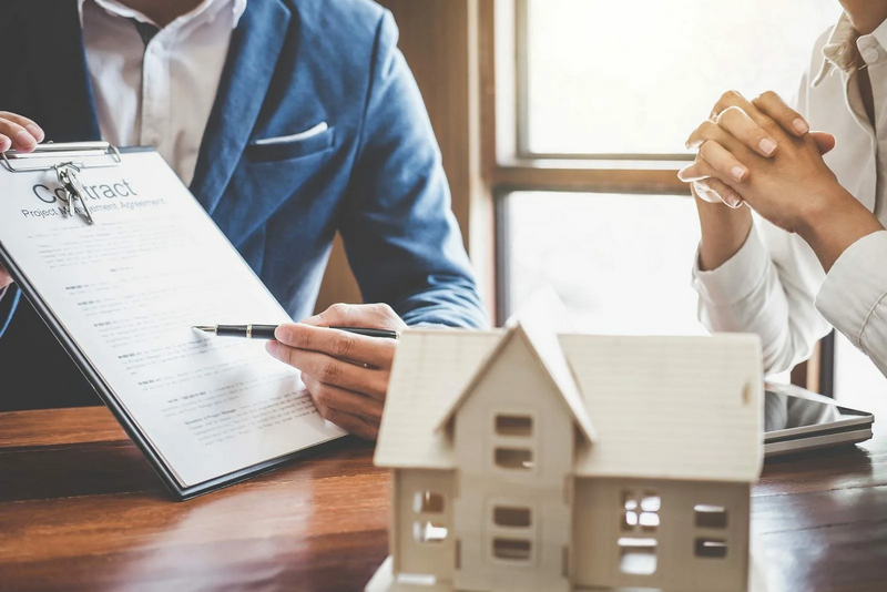 Two people are discussing a contract next to a small house model.