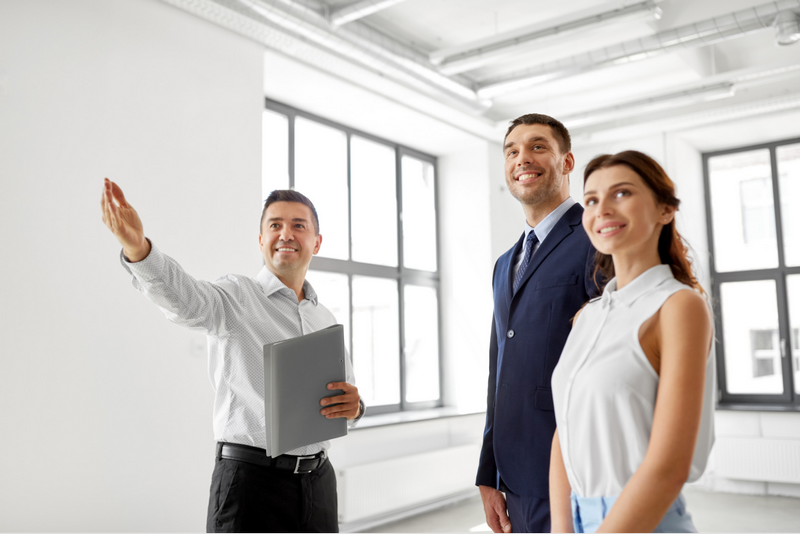 A real estate agent shows a modern apartment to a smiling couple.