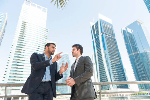 Two businessmen discussing rental options in front of modern skyscrapers in Binghatti Hills.